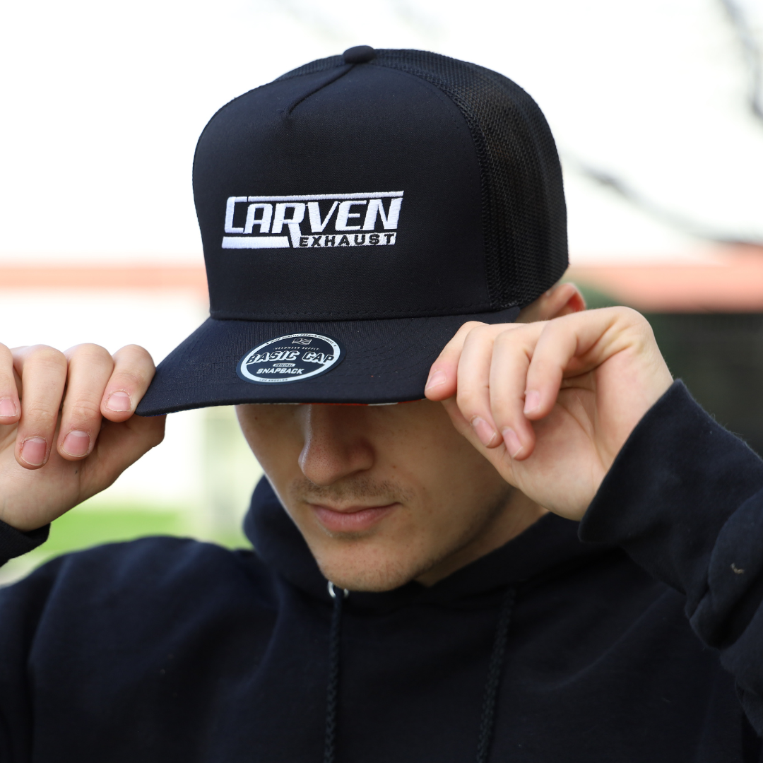 A man gripping the brim of a black hat with a white Carven Exhaust logo