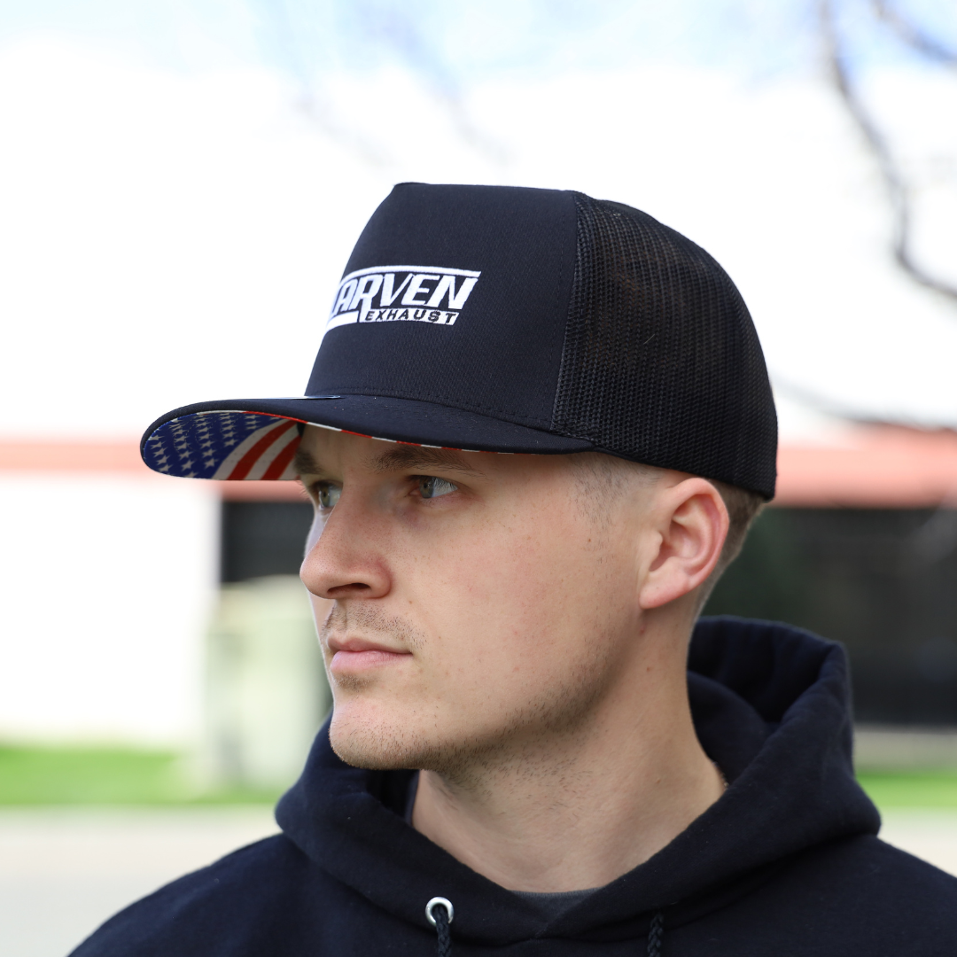 A man wearing a black hat with a white Carven Exhaust logo and an American flag brim