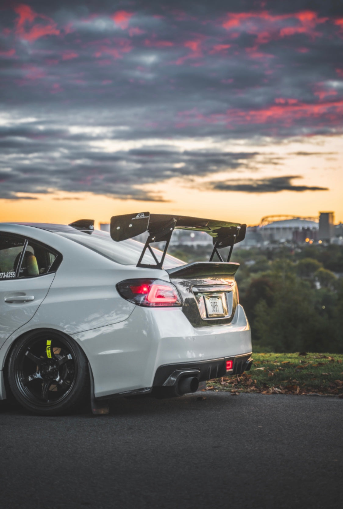 The backside of a parked white Subaru car with an installed 2015-2021 Subaru WRX & STI Carven Exhaust Single Exit Exhaust System and a sunset in the background