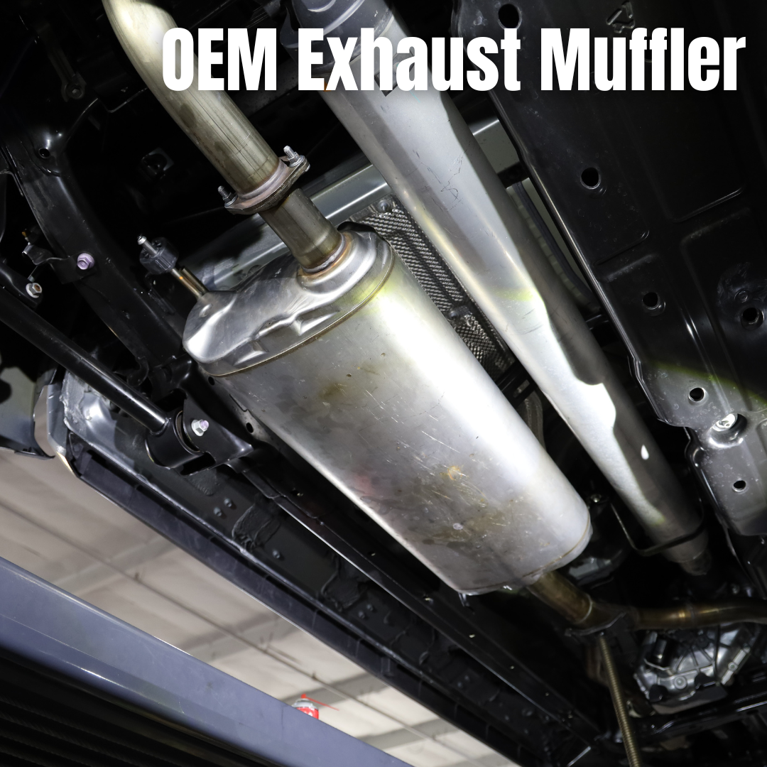 Close up of an installed OEM exhaust muffler on the underside of a vehicle with text that says "OEM Exhaust Muffler"