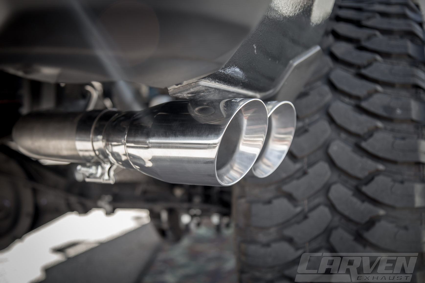 Side view close up of a 2010-2018 Silverado & Sierra 1500 Carven Exhaust PROGRESSIVE Series Cat-Back Exhaust Kit with a Polished stainless 4.0” Dual Exit Stainless Steel Tip installed on a truck