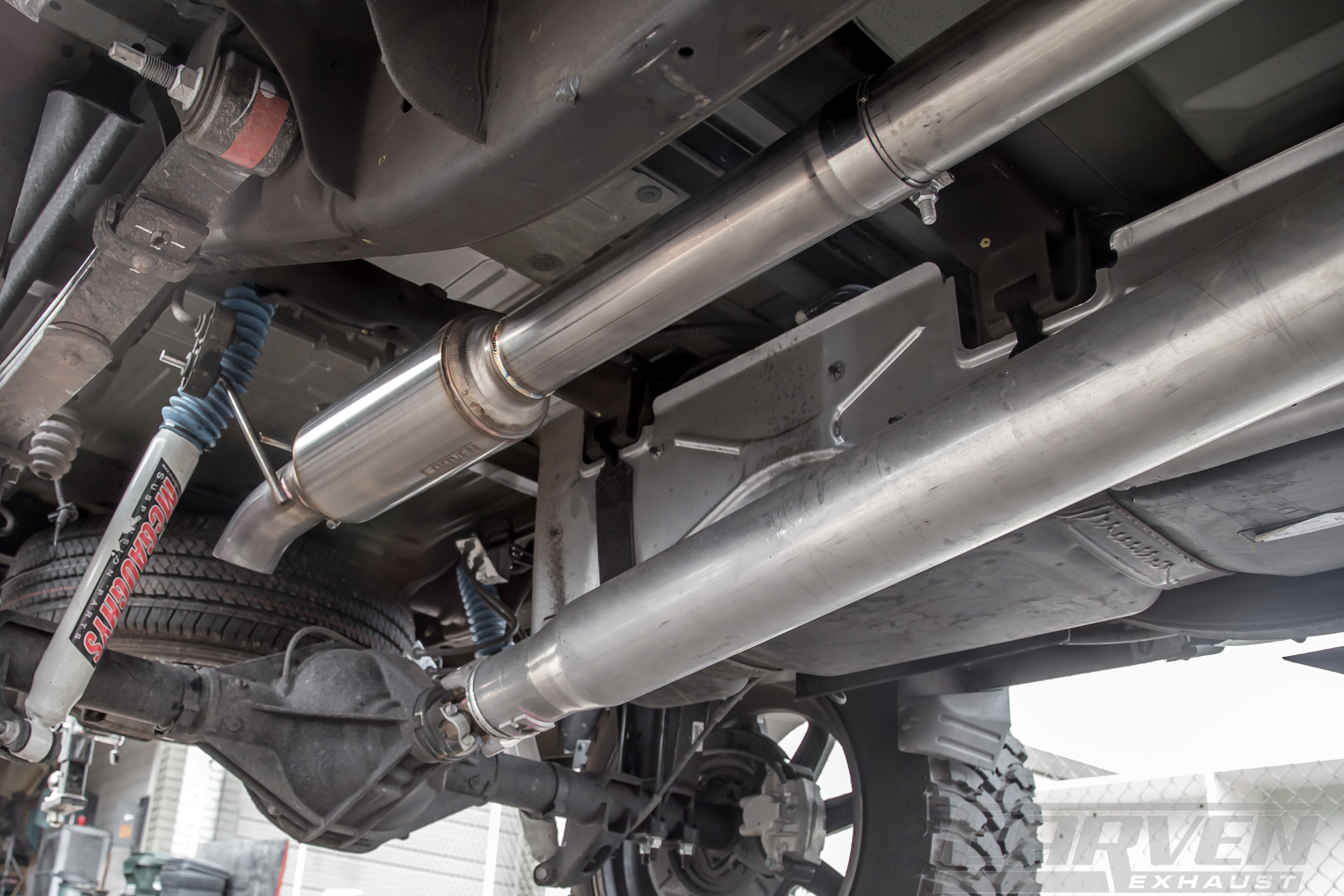 Wide angle of the underside of a truck showing an installed 2010-2024 Silverado & Sierra 1500 Carven Exhaust progressive Series Dump Exit System