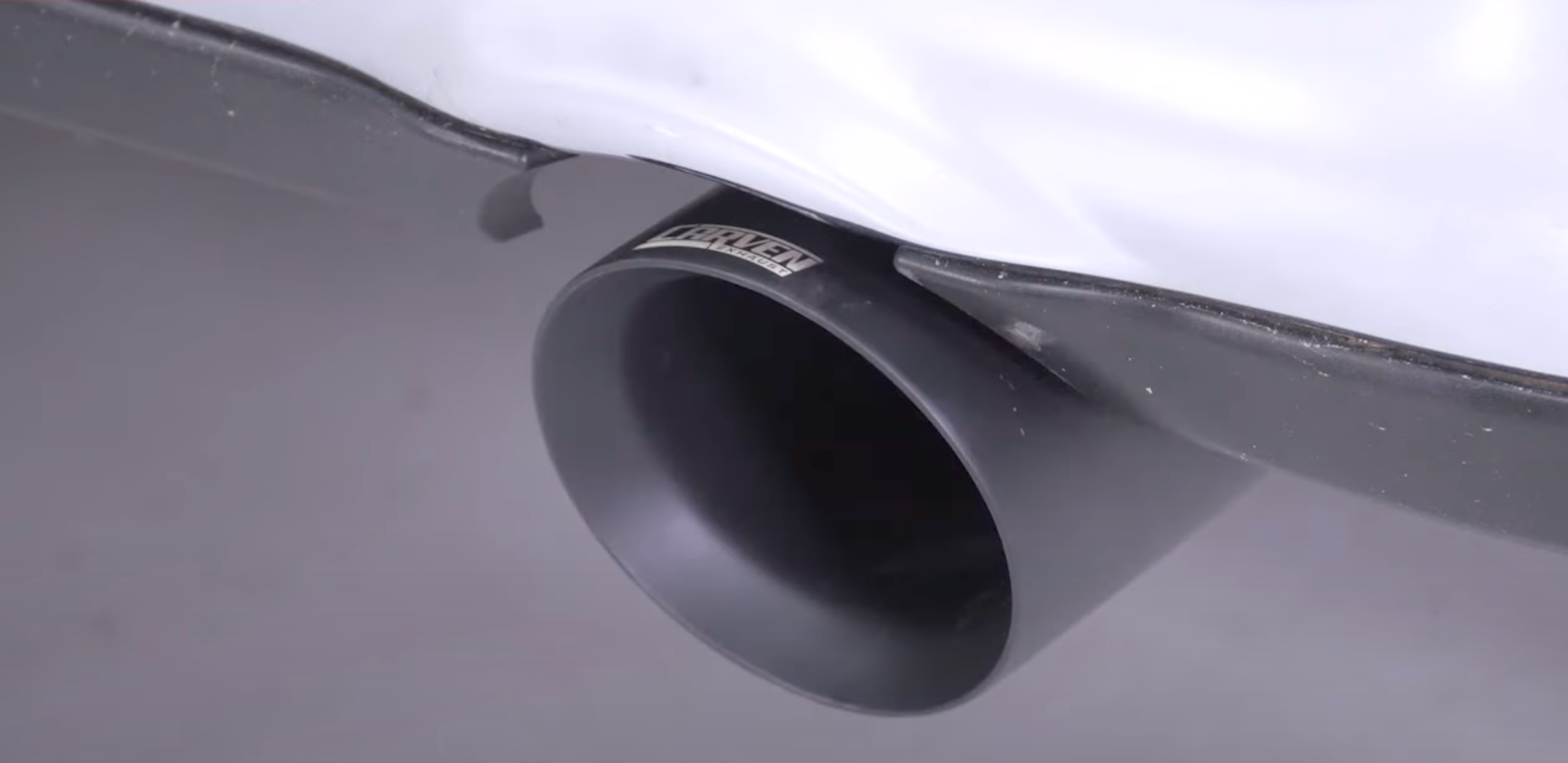 Close up of an installed 2009-2018 RAM 1500 Carven Exhaust 5.0" Direct Fit Bolt-On Exhaust Tip Replacement Set in the ceramic coated black color on a white vehicle