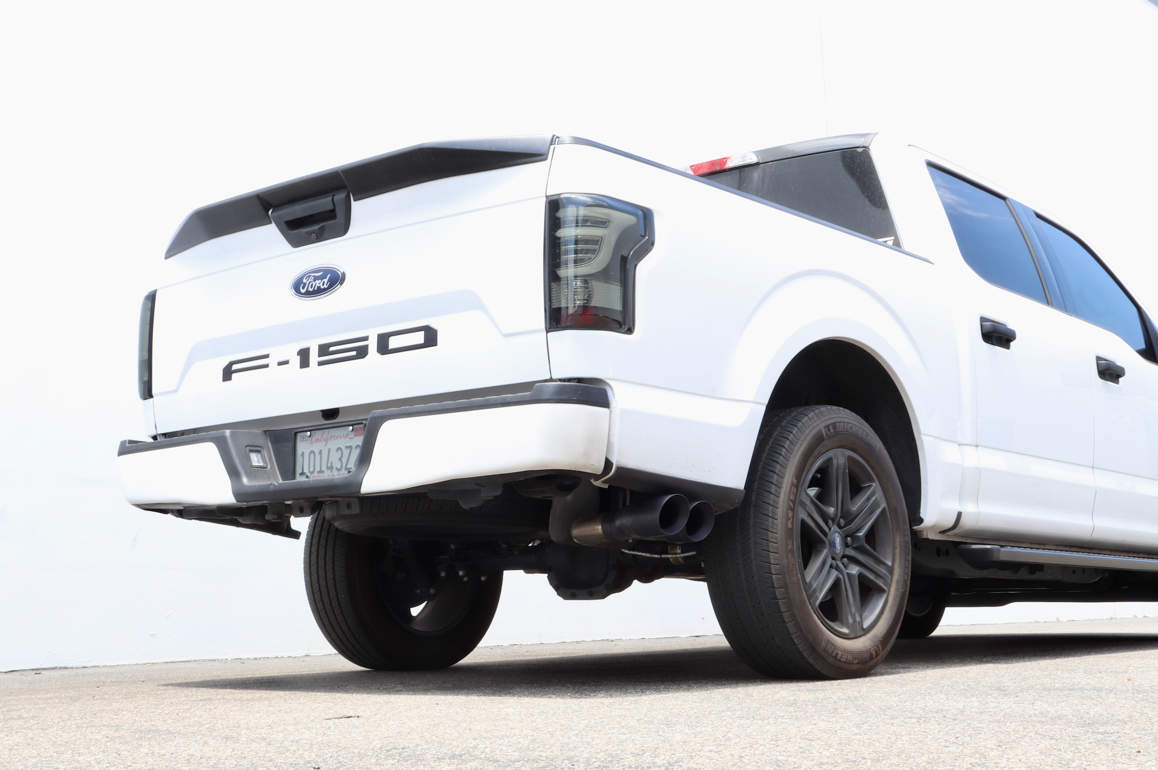 The backside of a white Ford F-150 truck with an installed V8 Carven Exhaust Cat-Back Kit with a Cerkaote black 4" Dual Exit Tip