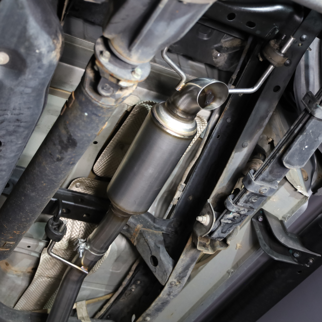 Underside of a car showing an installed 2005-2015 Toyota Tacoma 4.0L Short Bed Carven Exhaust Dump Exit Exhaust Kit