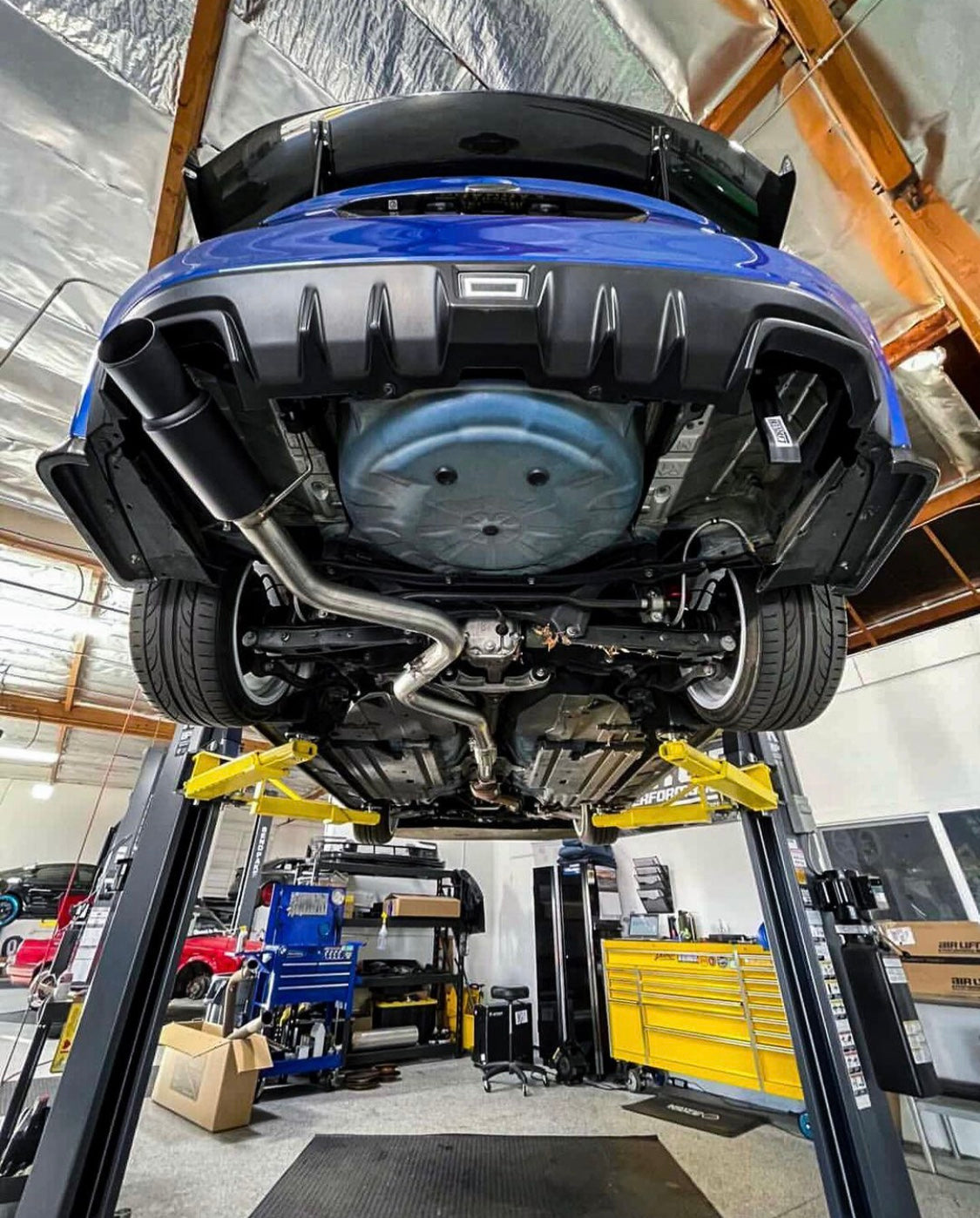 An elevated blue Subaru car with a 2015-2021 Subaru WRX & STI Carven Exhaust Single Exit Exhaust System with a ceramic coated black finish installed on the underside