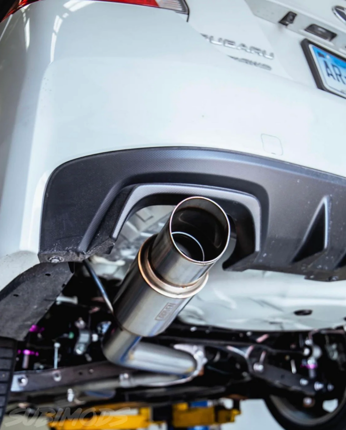 Close up of a 2015-2021 Subaru WRX & STI Carven Exhaust Single Exit Exhaust System with a polished stainless finish installed on a white Subaru car