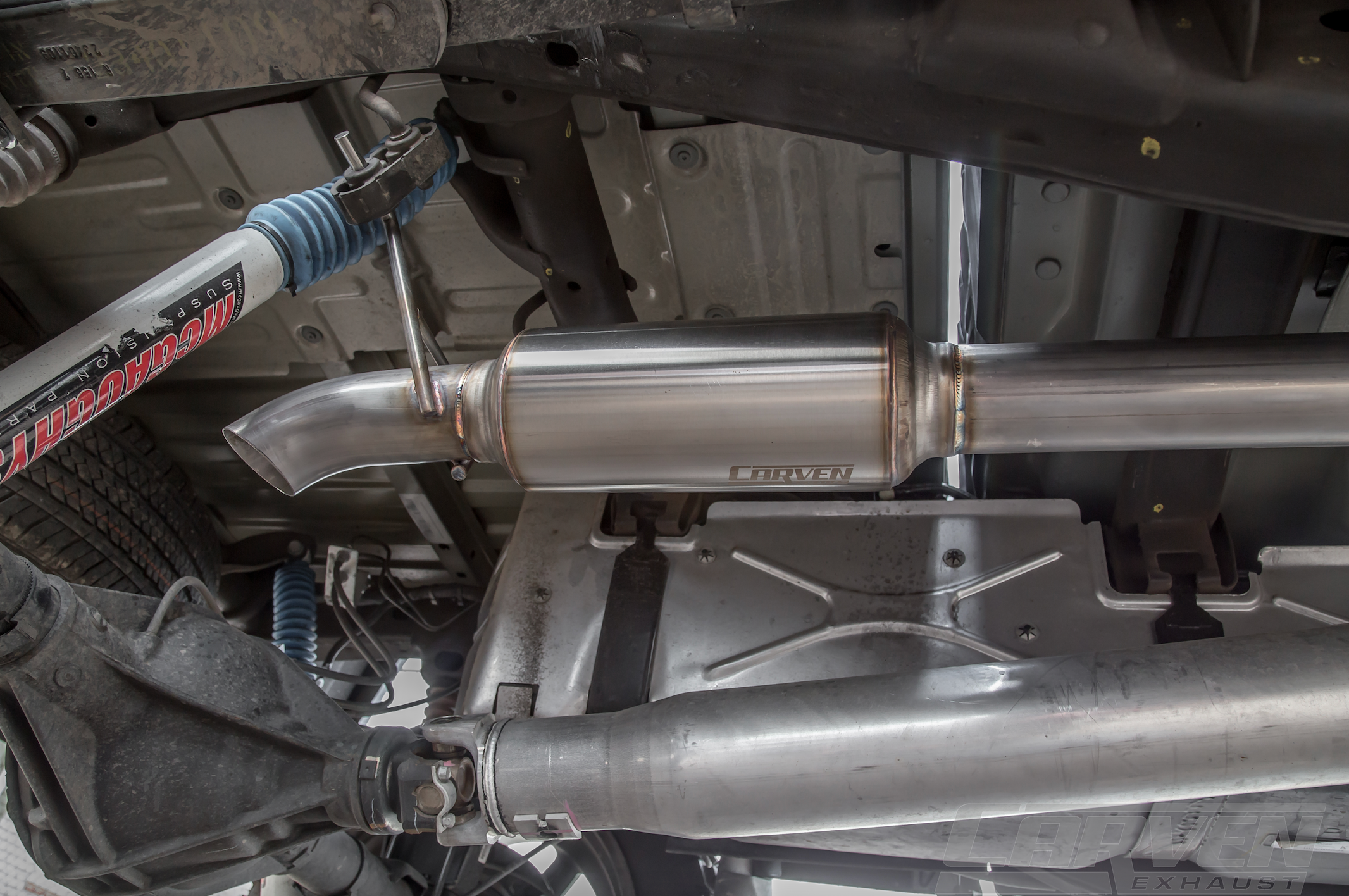 The underside of a truck showing an installed 2010-2024 Silverado & Sierra 1500 Carven Exhaust progressive Series Dump Exit System