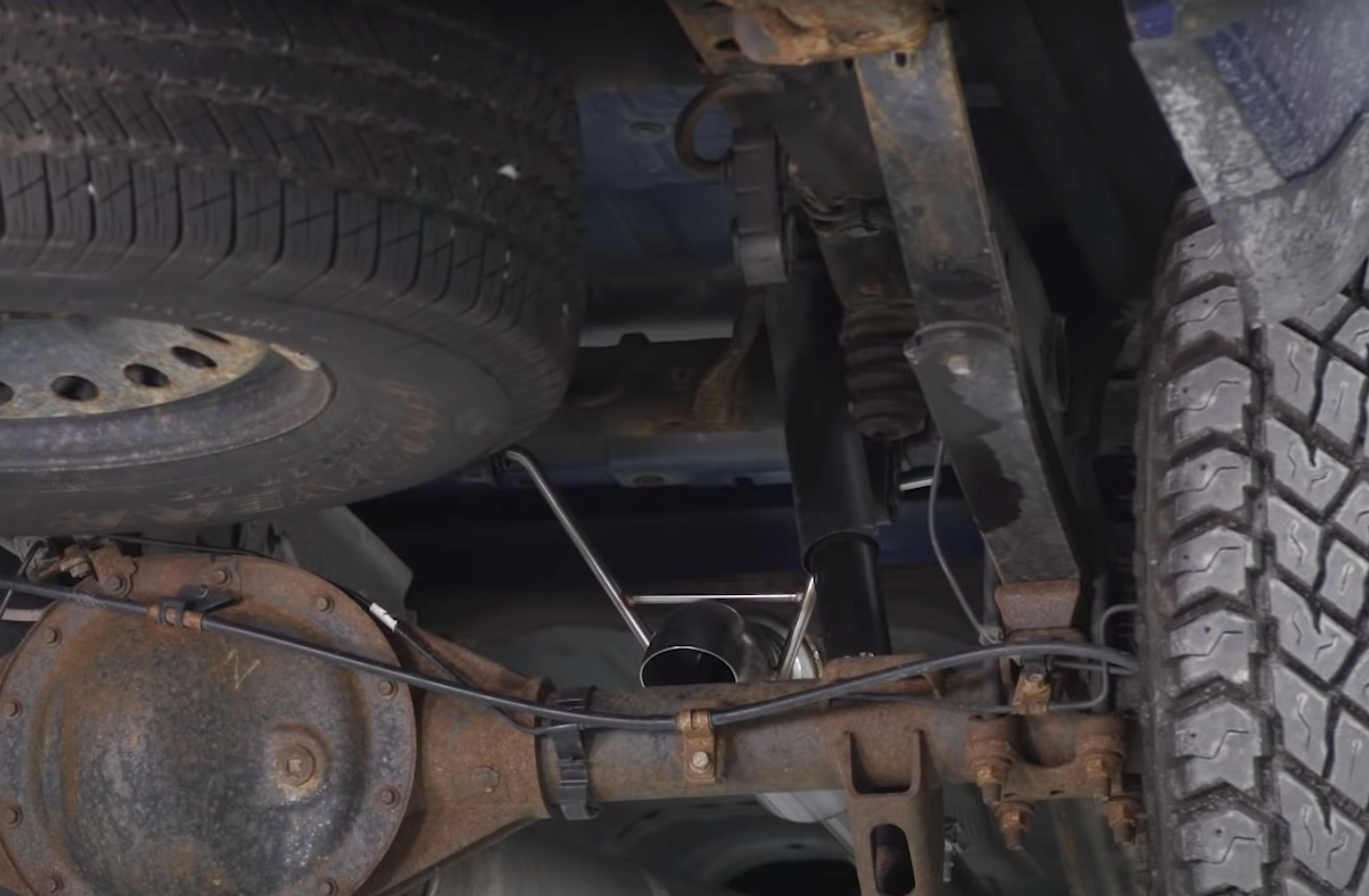 Close up of an installed 2010-2024 Silverado & Sierra 1500 Carven Exhaust Competitor Series Dump Exit Exhaust System on the underside of a truck