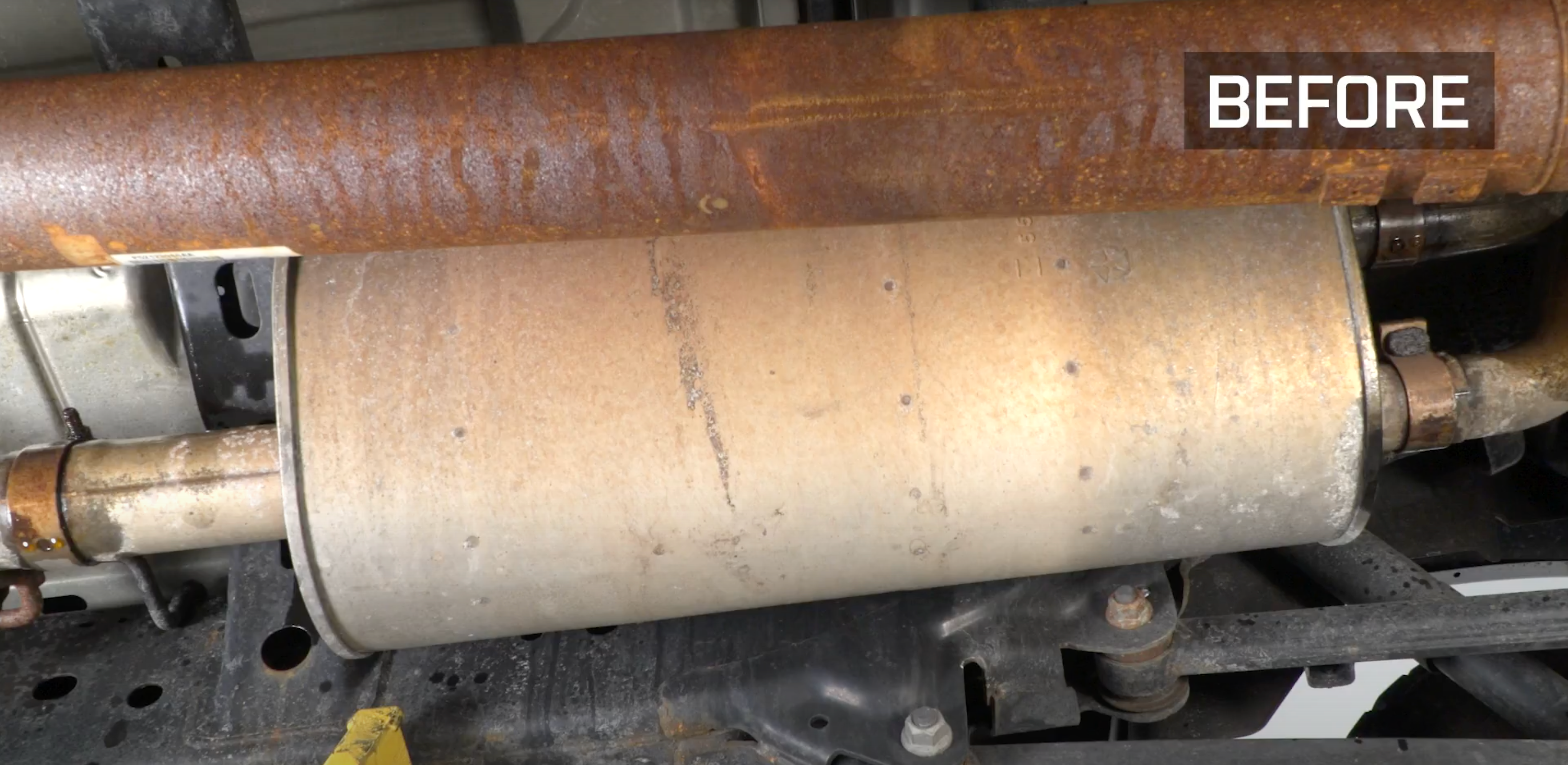 A muffler on the underside of a vehicle with a label in the corner with white text that says "Before"